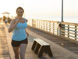 Overweight woman on pier in morning, running toward camera.